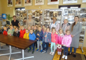 Grupa dzieci pozuje razem z panią dyrektor, panią Agnieszką, panią Anią oraz p. Dyrektor Miejsko- Gminnej Biblioteki Publicznej w Kleczewie Magdalena Siupa. W tle widać tablice zapełnione starymi fotografiami wsi.